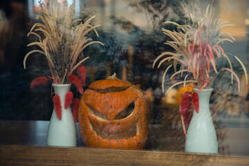 Bright orange Halloween scary pumpkin face emotions and vases in the window of the cafe, selective focus