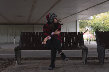 Young depressed homeless girl or woman sitting alone on the bench on the street under the bridge...