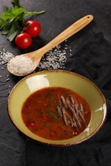 Georgian cuisine. Kharcho soup. Soup with veal, tomatoes, rice, hot pepper, ajika and fresh herbs in a beige plate on a black table. Wood spoon, fresh tomato. Restaurant. Background image, copy space