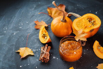 Fototapeta na wymiar Homemade pumpkin jam in a glass jar on the table with autumn maple leaves and fresh pumpkins