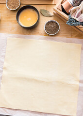 Quadrangular puff pastry deployed on a bakery paper.