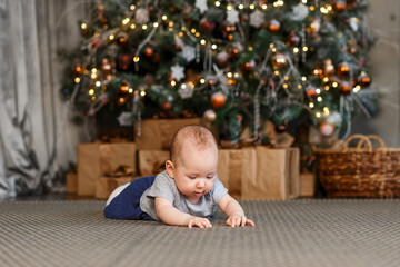 Fototapeta na wymiar Six-month-old baby girl lies on the floor near a beautiful Christmas tree. children's photo shoot