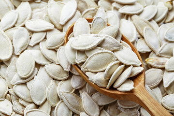 Full frame background texture of fresh pumpkin seeds with a rustic wooden spoon arranged diagonally on the surface.