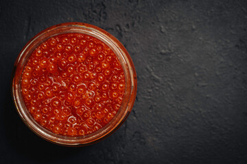 Red caviar in a glass bowl on a dark background. Top view, seafood, chum salmon caviar.