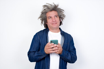 Image of a happy Handsome mature caucasian man with afro gray hair standing over white background listening to music with earphones using mobile phone.