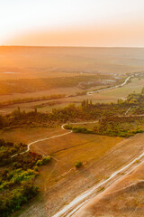 View from the height of the white rock and green valley in sunset orange lights. Blue sky, a small village at the bottom. Crimea