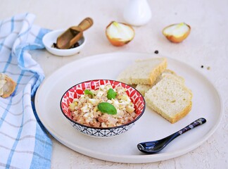Appetizer, salad of canned cod liver, boiled egg and onions in a colored ceramic bowl on a light concrete background. Served with fresh white bread.
