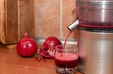 Pomegranate juice pours from a juicer into a glass. Making juice at home.