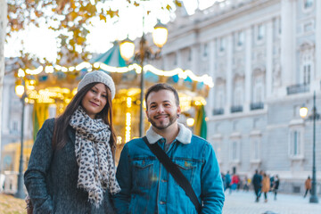 People visiting Europe 2020 city christmas lights in a carousel. Young couple smiling wearing a cap under the city christmas lights