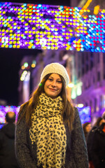 Girl visiting Europe 2020 city christmas lights. Women smiling wearing a cap under the city christmas lights