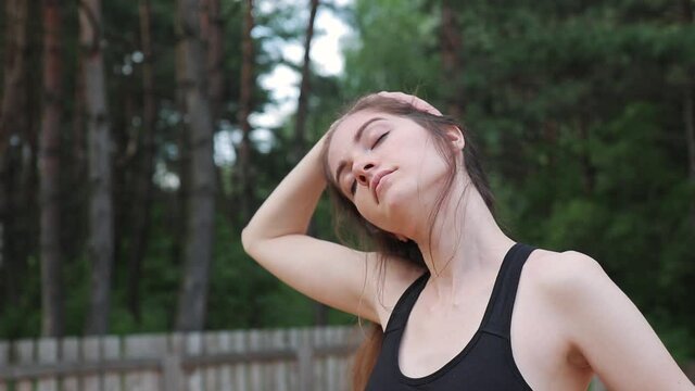 woman in black outfit works out in nature and stretches the neck muscles, close up