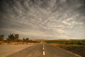 Cielo nuboso con altocúmulos y larga recta de carretera.