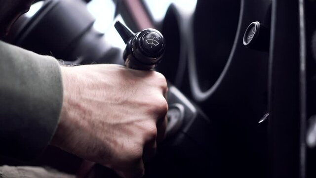 Male hand puts car key into socket and starts engine, colorful lights on control panel, close up. Footage. Starting old classic car motor.