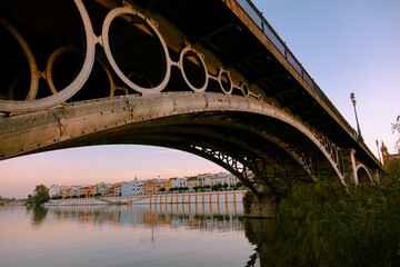 Atardecer sobre el puente de triana y calle betis al fondo reflejada en el río guadalquivir