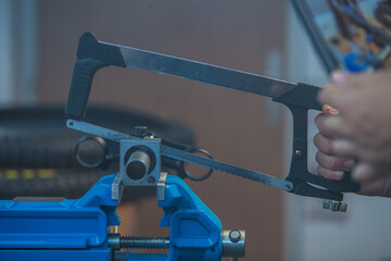 A man is holding a saw for metal and cutting through a pipe or steering tube of a bicycle while it is clamped in a vice.