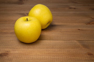 Two sweet and juicy yellow golden apples on a wooden table with empty space. Healthy snack concept.