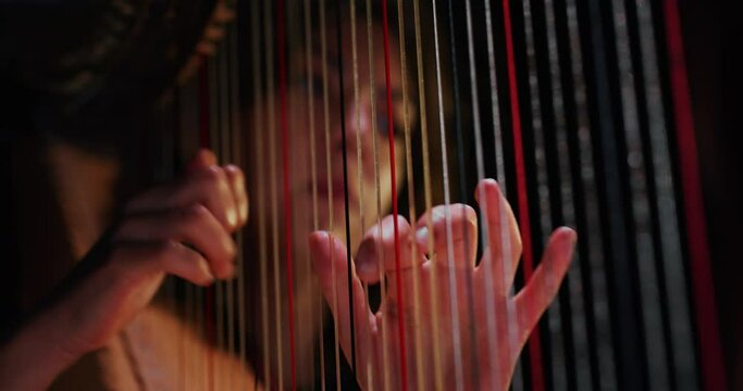 Cinematic close up shot of professional female harpist is playing harp solo on a classic theater stage with dramatic lighting before start a music concert.