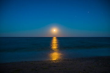 Fototapeta premium Landscape moon over horizon on sea and moonlight. Panorama with the luna of night. Lunar path on the water. Long exposure
