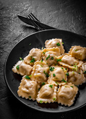 Meat dumplings - russian pelmeni, ravioli with meat in black plate on Dark grey black slate background
