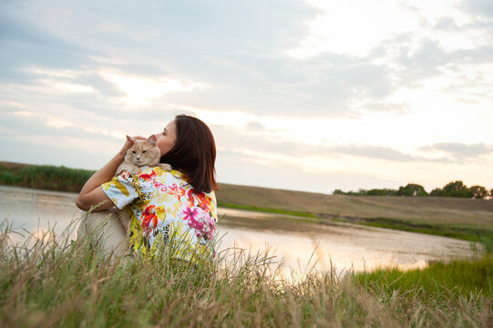 Photo of a woman hold a cat in a landscape with a little lake