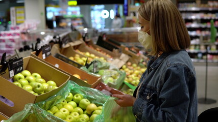 Young woman in mask picks apples in a bag in a store