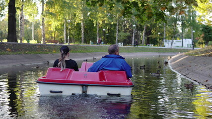 Adult man and woman ride a catamaran on the pond in the park