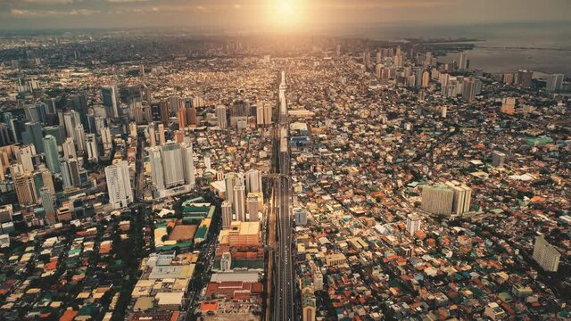Sun shine over city roofs of skyscrapers buildings aerial. Urban traffic road at streets of downtown. Philipines capital cityscape at summer sunlight. Filipino town cinematic soft light drone shot