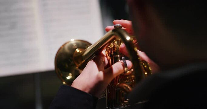 Cinematic close-up shot of male trumpet player during musical concert on classic theatre stage with symphony orchestra performing on background.