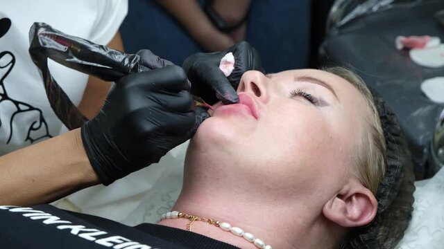 Cosmetologist making lips microblading permanent procedure using tattoo machine and pink pigment