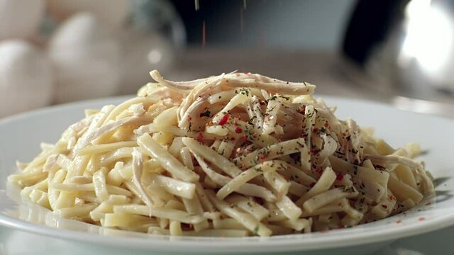Slow motion spice is thrown on the Turkish noodles on the serving plate. Close up.
