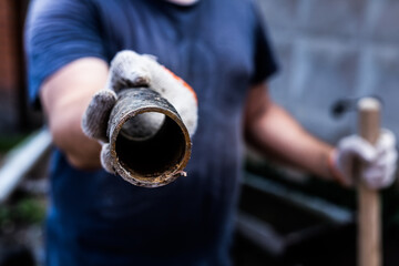 A worker holds in his hands piece of a metal pipe cut off