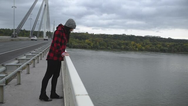 Young depressed homeless girl or woman standing alone on the bridge want to jump in to the water of the river and to commit suicide after hard life on the street