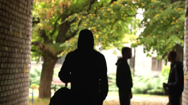 The athlete goes to training on the gateways, past the gopniks, hooligans, through the opening, passage, arch, corridor, house. Autumn. In black clothes, sports sweatshirt. Back view
