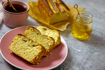 Banana cake gluten free and sugar free for breakfast. Pieces of banana bread on a pink plate on a gray table, next to a cup of tea, honey. Healthy nutrition concept