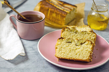 Banana cake gluten free and sugar free for breakfast. Pieces of banana bread on a pink plate on a gray table, next to a cup of tea, honey. Healthy nutrition concept