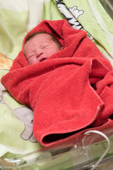Dark-haired baby after birth wrapped in a red towel.