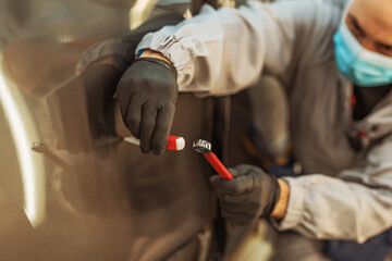 A car factory worker wearing a protective medical mask removes a metal defect with a hand tool.