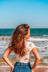 Fototapeta na wymiar Happy woman with long hair standing on the beach in front of the blue sea or ocean, the concept of the elements and freedom