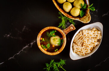 Matzo ball soup in two plates with spoons on black background.