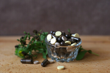 Herbal pills in a glass plate on brown background. Phytotherapy. Herbal treatment Natural medicines