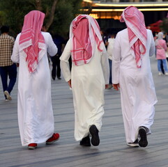 Drei Emiratis mit langen weißen Gewändern und rotem Kopftuch
