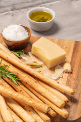 Traditional italian breadsticks grissini with rosemary, parmesan cheese, olive oil, garlic and salt on a gray background.