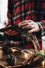 Making of Christmas wreath from nature materials on a dark wooden table. Scandinavian hygge styled Christmas composition. Cozy winter homely scene with decorations.