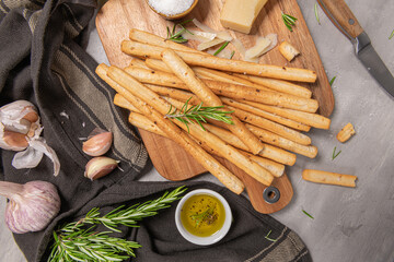 Traditional italian breadsticks grissini with rosemary, parmesan cheese, olive oil, garlic and salt on a gray background. top view. Flat lay with copy space