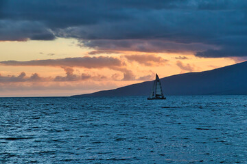 Moody sunset of a sailboat in Lahaina harbor with Lanai in the distance.