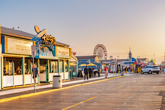 Santa Monica, California - October 09 2019: Rusty's Surf Ranch restaurant Santa Monica Pier & Beach open for business. People/ tourists walk by vendors and Police Station. Ferris wheel in background.