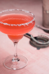 Red Margarita cocktail and some bartender accessories on a pink background