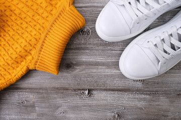 Yellow warm pullover for cold autumn and winter weather with white casual leather sneakers on wooden background, copy space, flat lay