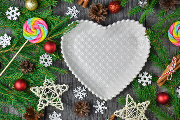 White plate in the shape of a heart on the background of fir branches and Christmas decorations. Merry Christmas