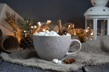 Large coffee mug with marshmallows and spices on the background of Christmas lights